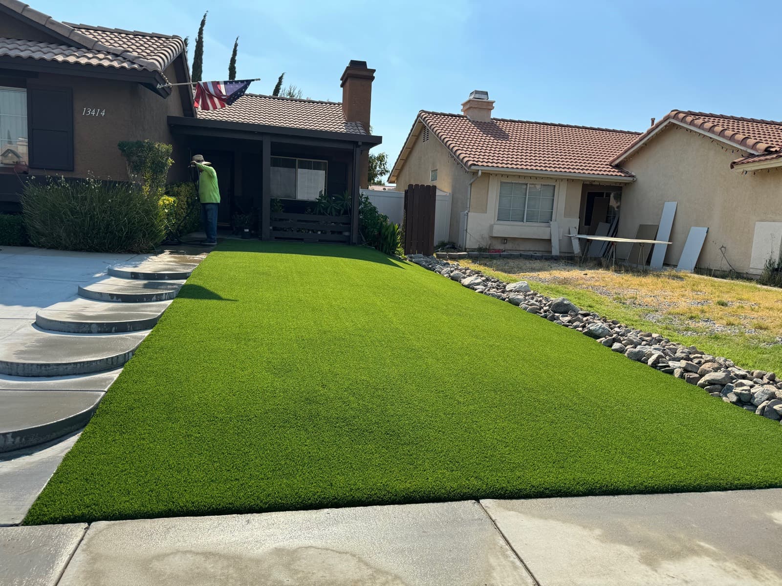 Front-yard turf lawn next to a concrete driveway and rock border