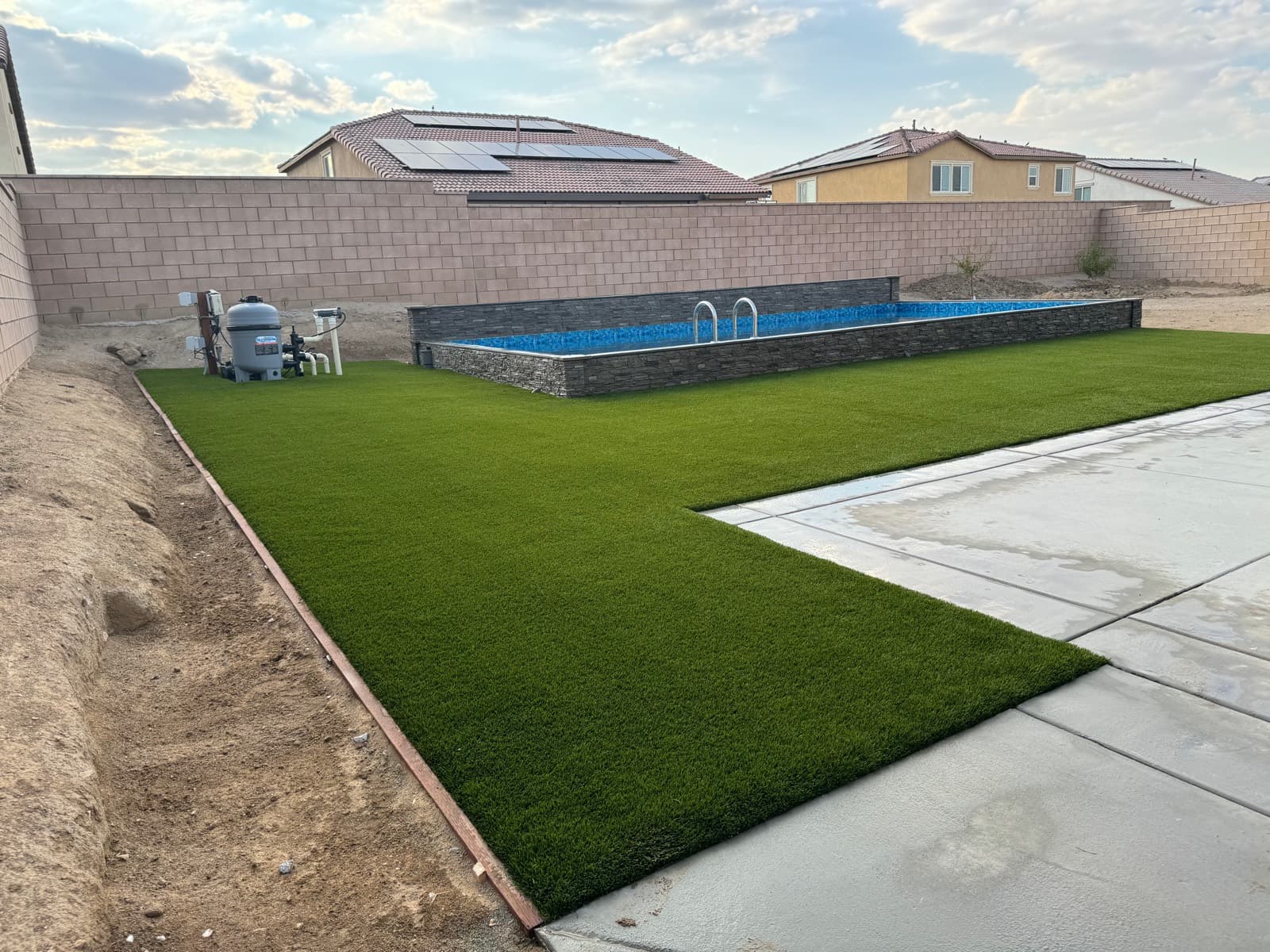 Turf lawn around an above-ground pool with a stone base