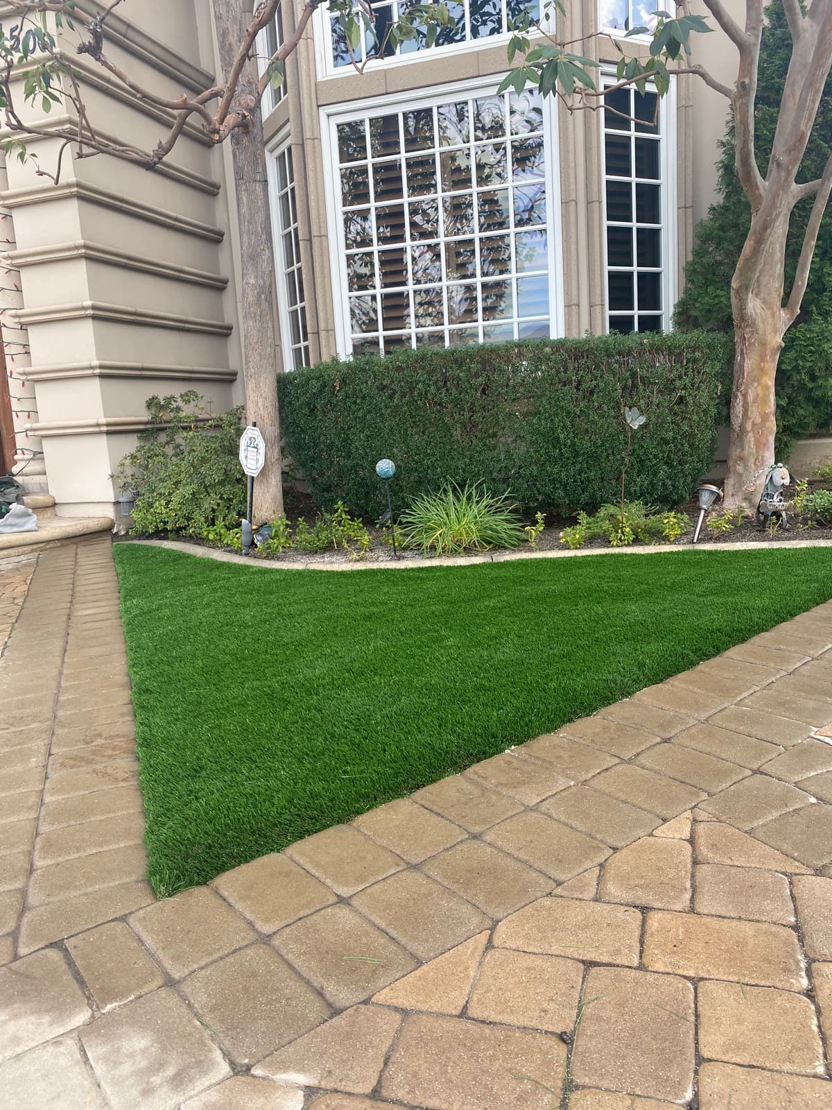 Small triangular turf panel set in tan pavers at a house entry