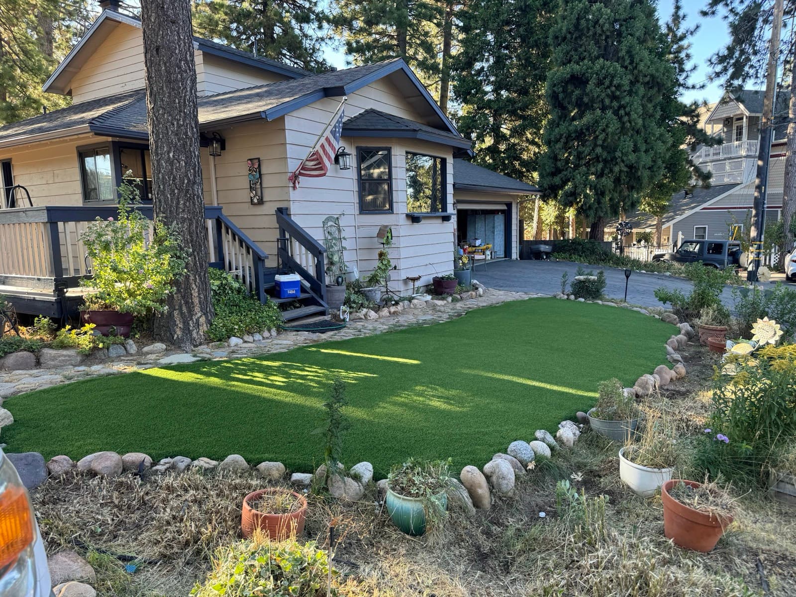 Oval turf lawn edged with river rock in a wooded front yard