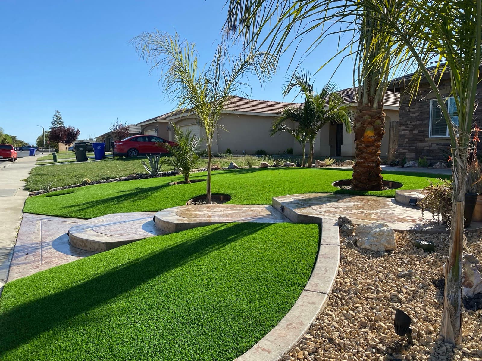Front-yard turf with palm trees, circular concrete pads, and gravel