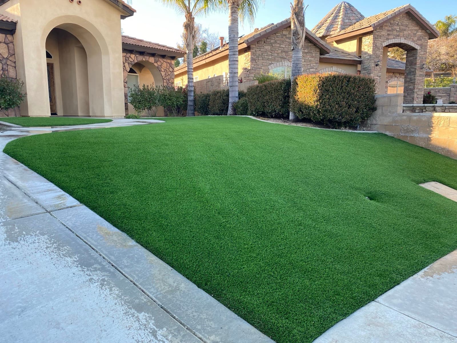 Curved front-yard turf lawn in front of a stucco house with stone accents