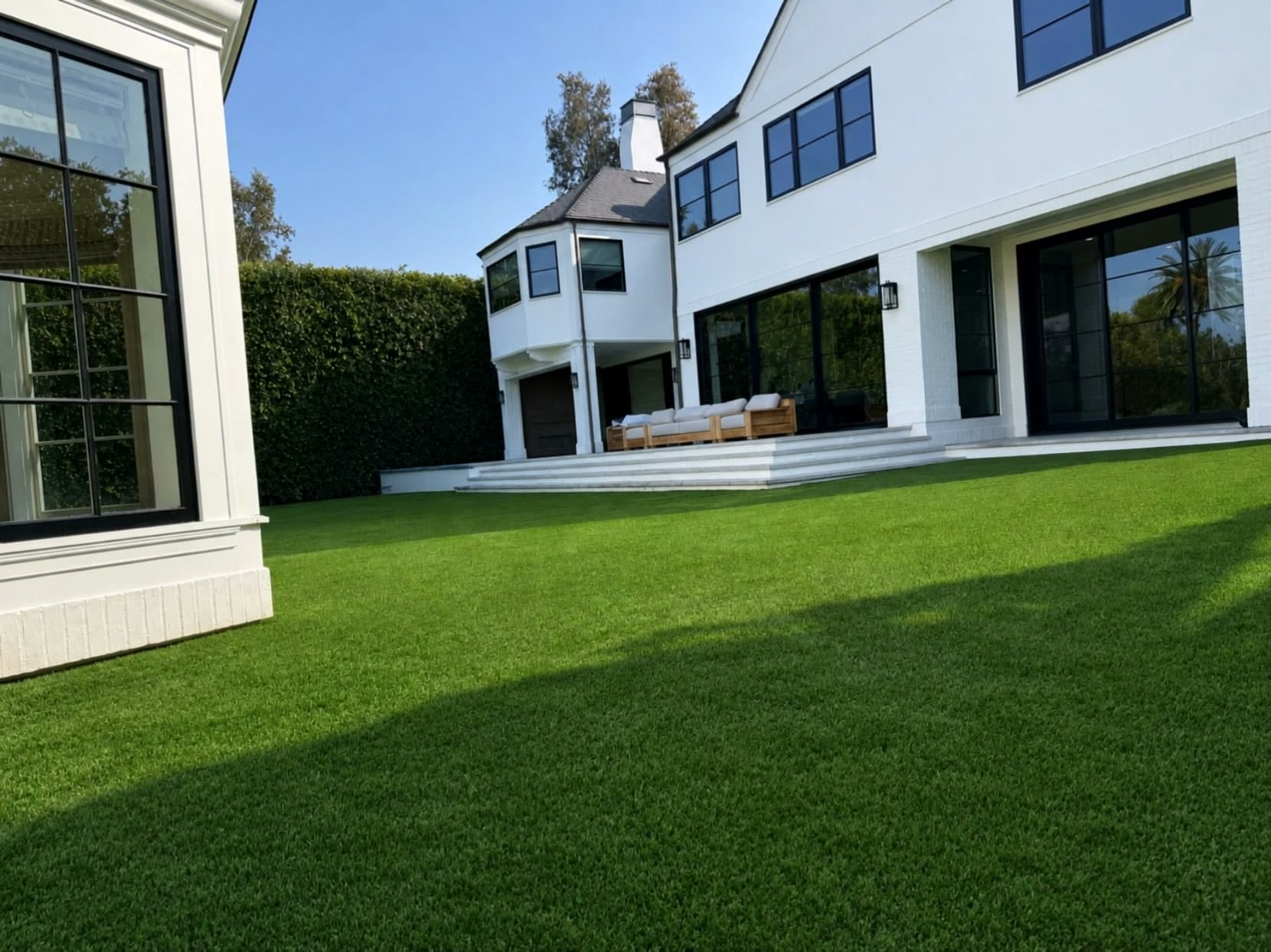 Finished backyard lawn of dense green turf in front of a white house